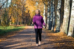an elderly woman walks through the Park on Scandinavian sticks