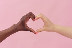 Caucasian woman and African American man show heart with their hands on pink background. The concept of racism, tolerance