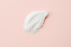 Cleansing foam for face, hands or body. Face cleansing mousse sample texture closeup.. White cleanser foam bubbles on pastel pink background.
