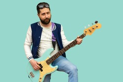 Blond boy wearing t-shirt and blue jeans with sunglasses on his head playing a beautiful bass on a light blue background