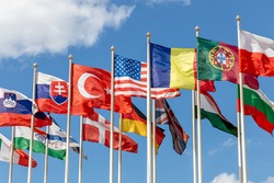 Group of flags of various states - as a symbol of world cooperation. Flags of the countries of the world on flagpoles flutter in the wind against the background of a blue sky
