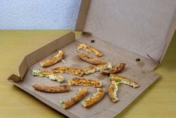 Pizza crusts in a greasy box on a home table. Leftover pieces of pizza. High-calorie food