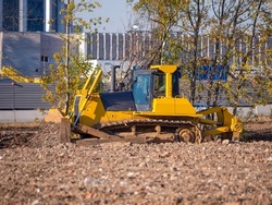 Yellow crawler bulldozer with blade and plow working at a construction site. Site preparation for the construction of buildings and structures. Heavy construction equipment