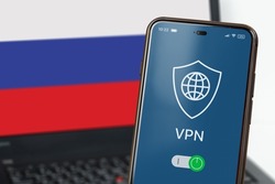 VPN in Russia. A smartphone with VPN turned on in the foreground and a laptop screen with the flag of Russia in the background. Using VPN on cell phone and computer. Selected focus