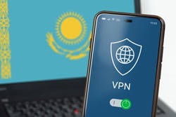 VPN in Kazakhstan. A smartphone with VPN enabled in the foreground and a laptop screen with the flag of Kazakhstan in the background. Using VPN on mobile phone and computer. Selected Focus