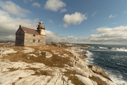 Historic lighthouse, ocean view, stone building double story, slate roof, a walkway around the light room gives the impression of a castle, sits on a rocky shore of the Atlantic ocean,