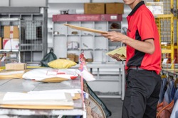 Thai young postal man is sorting mail parcels at postal office.