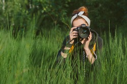 A girl photographer is holding a professional photo-video camera in her hands. Against the backdrop of beautiful green nature and forests