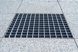Close-up, metal cover of street water drain. Against the background of paving slabs of gray granite