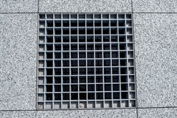 Close-up, metal cover of street water drain. Against the background of paving slabs of gray granite. View from above