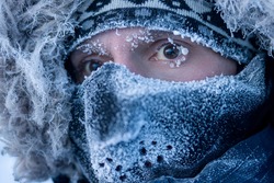 Portrait of a man in winter clothes and a mask. A traveler in the Arctic. Ice and snow on eyelashes, face and mask. Cold polar climate. Extreme travel and expeditions to the far North to the Arctic.