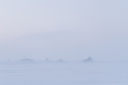 Winter arctic landscape. View of houses in the snowy tundra. Poor visibility in frosty fog and during a blowing snowstorm. Abandoned buildings in the Arctic. Chukotka, Siberia, the Far North of Russia