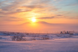 Beautiful winter sunset in the Arctic. View of the snowy tundra and the setting sun over the mountains. Cold frosty winter weather. Blowing snow. Satellite dishes in the tundra. Chukotka, Russia.