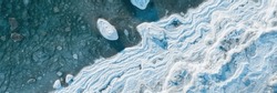 Top view of the icy seashore. Winter aerial photograph of the sea coast. Ice floes in freezing sea water. Nature of the Extreme North and the Arctic. Cold frosty winter weather. Natural background.