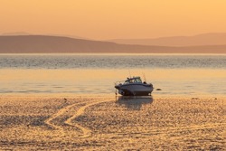 Boat on the shallows at low tide. Morning seascape at sunrise. View of the shallows, sea bay and mountains. Golden morning sunlight at dawn. Beautiful natural background.