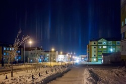 Night cityscape. View of a snow-covered street in the northern city. Bright pillars of light in the frosty sky. Cold winter weather. City of Anadyr, Chukotka, Siberia, Far North of Russia. Arctic.