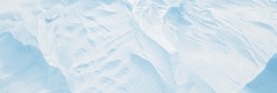 Wide panoramic winter background with snowy ground. Natural snow texture. Wind sculpted patterns on snow surface. Arctic, Polar region.