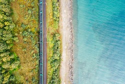 Lake Baikal shore with green forest trees and turquoise water, aerial top down view. Freight train with coal on railroad of Trans-Siberian Railway. East Siberian Railway in Buryatia, Siberia, Russia