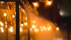 Bokeh photography of restaurant lights. Focus placed on a single lightbulb, and the surroundings are completely defocused for an ambient capture. Water steam from the roof creates a unique look.