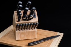 Set of Kitchen knives in a knife block with the chef knife laying on a cutting board, isolated on a black background