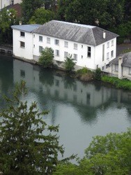 Gave de Pau river flowing through Lourdes with a town's building by the river bank. Hautes-Pyrenees, Occitanie, Southwest France