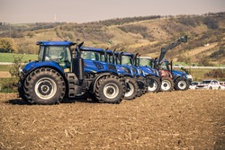 Close-up photo of a row of modern big tractors standing in the field during sunny autumn day. Tractor dealership event with presentation of front loader.
