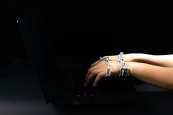 Freedom of the press and journalism, conceptual image Laptop and woman hand tied with chains can not typing keyboard on black background. World press freedom day. Copy space for advertisers.