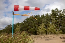 Windsock on a sandy beach in strong wind, Red and white fabric cone designed to indicate the direction and approximate wind speed, coastline, dense green forest