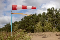 Windsock on a sandy beach in strong wind, Red and white fabric cone designed to indicate the direction and approximate wind speed, coastline, dense green forest