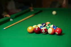 billiard cues and pyramid of multicolored pool balls on green billiard table