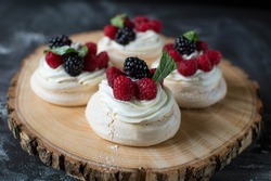 Mini Pavlova with raspberry and blueberry on a wooden plate with black background