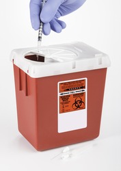 A gloved hand inserting Medical and/or Dental waste into a medium size Sharps container. White background.