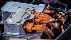 Powerful orange cables connecting the electric vehicle engine, inverter, traction battery and air conditioning compressor. EV maintenance concept.