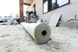 A roll of synthetic construction fabric is located at a construction site. Foreground