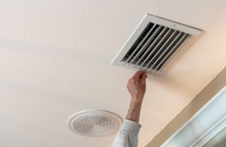 Handyman adjusting HVAC ceiling air vent. Air flow adjustment for overhead home heat and air conditioning ventilation duct.