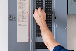 Resetting tripped breaker in residential electricity power panel. Male electrician turning off power for electrical outlet at circuit breaker box.