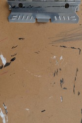 Brown cardboard texture of a drawing board / clipboard for artists that has black and white paint and scratches and other misc markings.