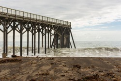 Waves breaking on the poles under the pier of San Simeon, California, USA