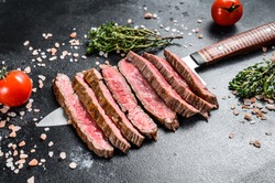 Grilled and sliced flat iron rare steak. Marble beef meat. Black background. Top view