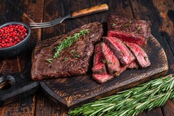Grilled sliced skirt beef meat steak on a cutting board with herbs. Dark wooden background. Top view