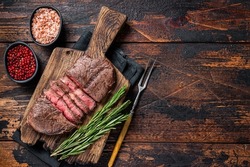 Fried Top Blade or flat iron roast beef meat steaks on wooden board with rosemary. Dark wooden background. Top View. Copy space