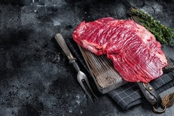 Uncooked Raw Flank or flap beef steak on butcher board. Black background. Top view. Copy space