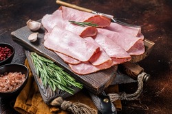 Flat slices of square sandwich ham with herbs. Dark background. Top view