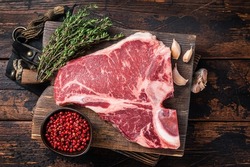 Prime T-bone beef meat steak, raw porterhouse steak on butcher board with herbs. Wooden background. Top view.