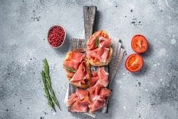 Spanish Tapas - Toast with tomatoes and cured Slices of jamon iberico ham on wooden board. Gray background. Top view.