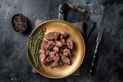 Chopped Grilled Diced Beef garlic steak on a plate with thyme. Black background. Top view