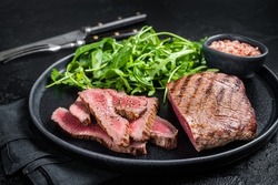 BBQ grilled Skirt Steak on a plate with green salad. Black background. Top view.