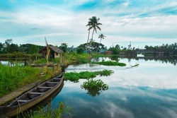 Wooden Boat In Backwater, typical landscape with palm trees and old hut,  Kerala backwaters photography during day time Kadamakkudy Kerala, Stripe of coconut trees between a cloudy sky and river.