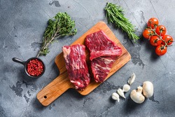 Raw flap steak flank cut with Machete, Skirt Steak, on woods chopping board, with herbs tomatoes peppercorns over grey stone surface background top view