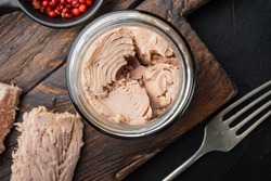 Canned tuna fillet meat in olive oil, on black background, flat lay